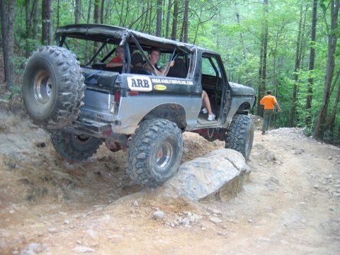 1992 Ford Mustang - Modified Ford Bronco tackling a challenging off-road trail with large tires and a spare tire on the back.