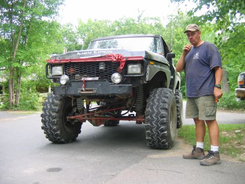 1992 Ford Mustang - A man stands next to a custom-built, lifted pickup truck with off-road tires and a prominent red grille guard.