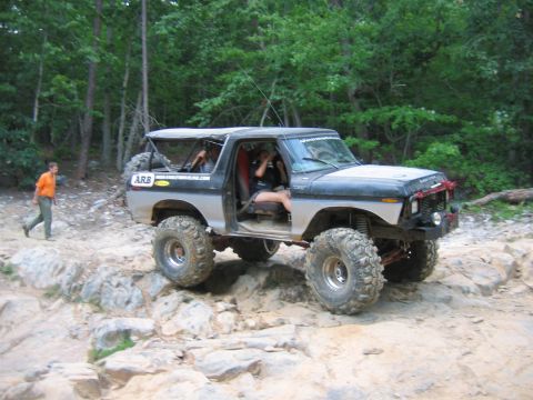 1992 Ford Mustang - A modified Ford Bronco navigates a challenging rocky terrain with a person walking nearby.