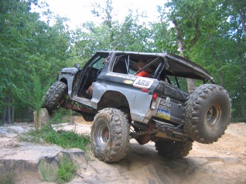 1992 Ford Mustang - This heavily modified SUV is navigating a challenging off-road course with its tires elevated on rocks.