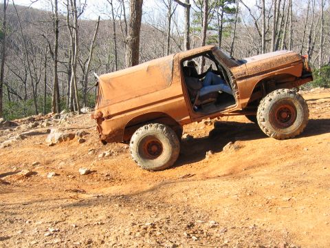 1992 Ford Mustang - An orange off-road SUV navigates a steep dirt incline amidst a wooded area.