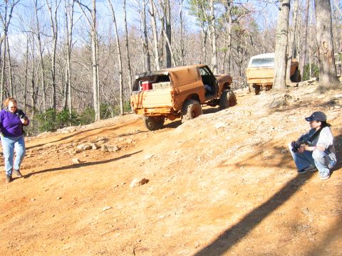 1992 Ford Mustang - Two off-road vehicles are seen on a dirt trail in a wooded area, with two people observing.