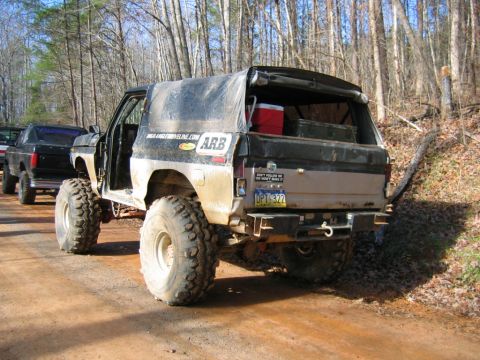1992 Ford Mustang - Modified SUV with large off-road tires and a soft top, parked on a dirt road with another truck behind it.