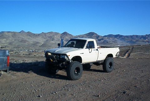 1986 Ford Bronco - A modified white pickup truck sits in a dry, mountainous terrain under a clear blue sky.