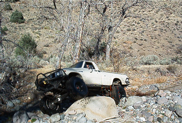 White pickup truck with large tires climbing over rocks on a trail