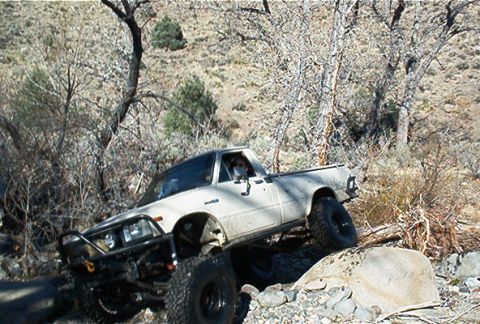 1986 Ford Bronco - A modified white pickup truck is shown off-roading on a rocky trail.