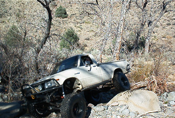 White pickup truck with off-road modifications navigating rocky terrain