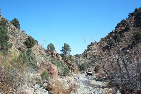 1986 Ford Bronco - A white SUV navigates a , rocky trail through a dry canyon under a clear blue sky.