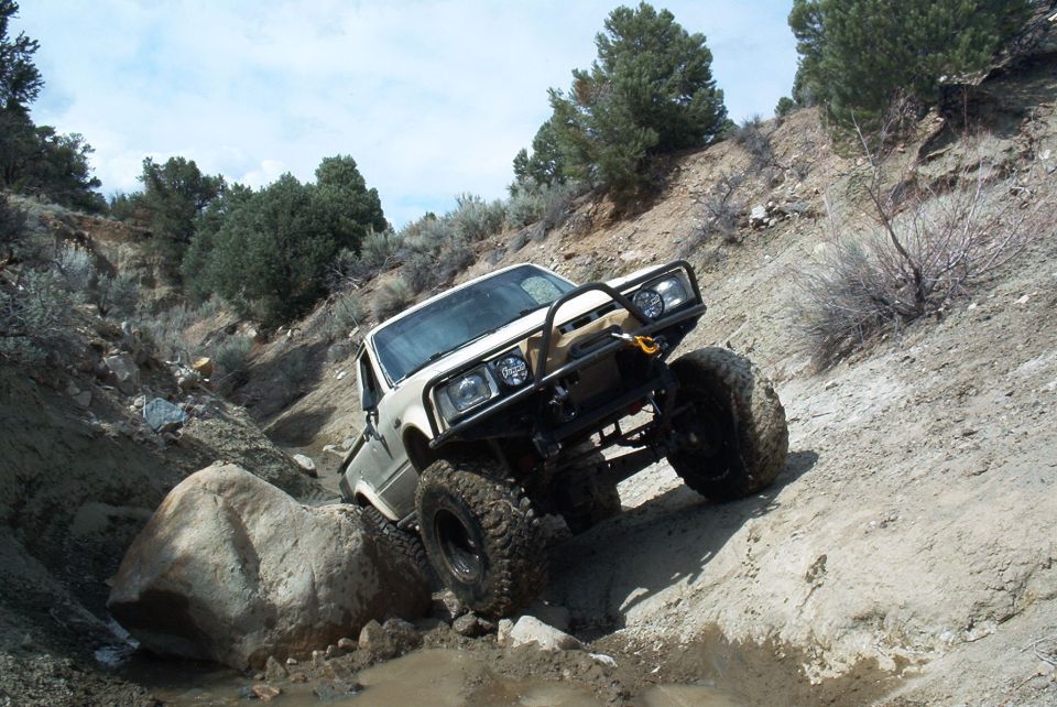 White off-road truck with large tires climbing a rocky incline