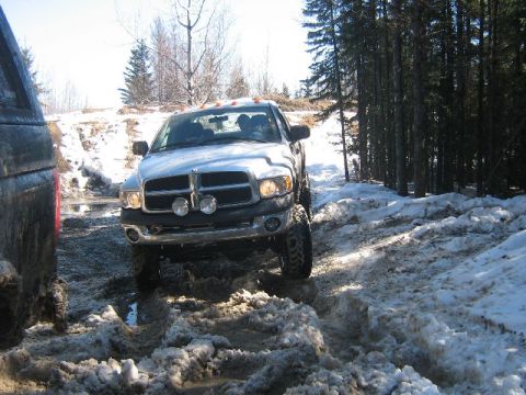 1995 Ford Bronco - Silver Dodge Ram pickup truck driving off-road on a snowy and muddy trail.