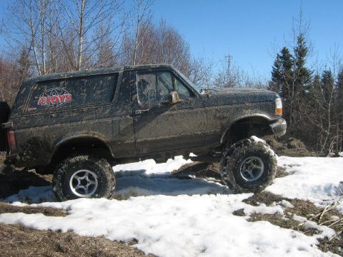1995 Ford Bronco - This lifted SUV navigates a snowy, muddy terrain, showing off its off-road capabilities.