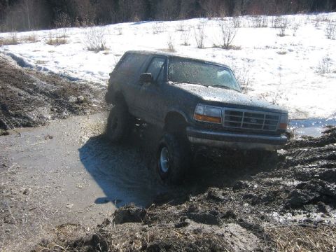 1995 Ford Bronco - This 1995 Ford Bronco is navigating a challenging off-road path with mud and snow.