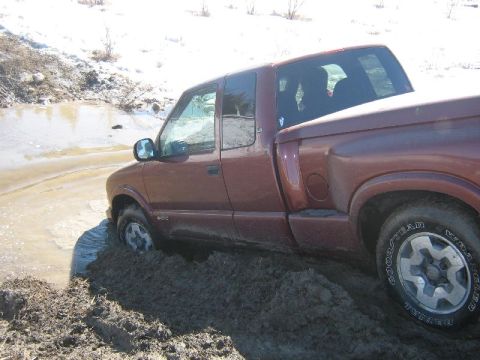 1995 Ford Bronco - A maroon pickup truck is stuck in a muddy, watery area with snow in the background.