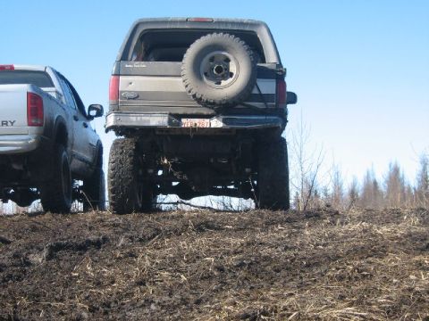 1995 Ford Bronco - Rear view of a lifted 1995 Ford Bronco with a spare tire mounted on the tailgate, parked next to another truck.