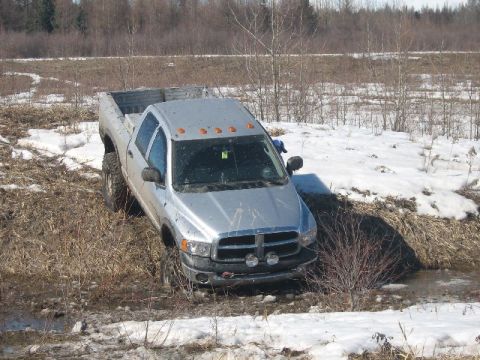 1995 Ford Bronco - Silver Dodge Ram pickup truck stuck in mud and snow off-road.