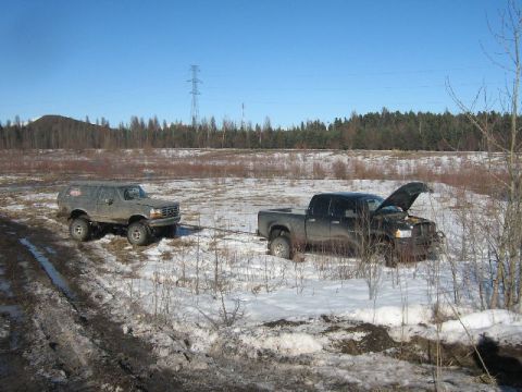 1995 Ford Bronco - A 1995 Ford Bronco is being towed by a black pickup truck in a snowy, wooded area.