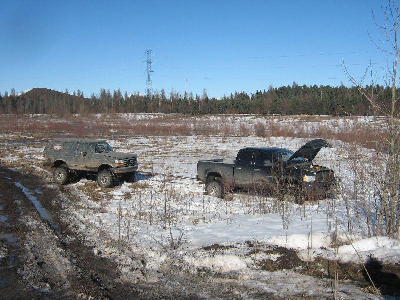 1995 Ford Bronco being towed by a black pickup truck in a snowy field
