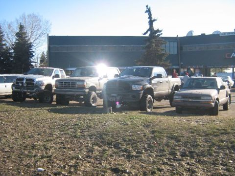 1995 Ford Bronco - Several modified trucks and SUVs are parked in front of a building on a sunny day.
