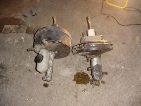 1992 Ford Bronco - Two brake booster and master cylinder assemblies laid side by side on a concrete garage floor for comparison. The left unit has a transluce…