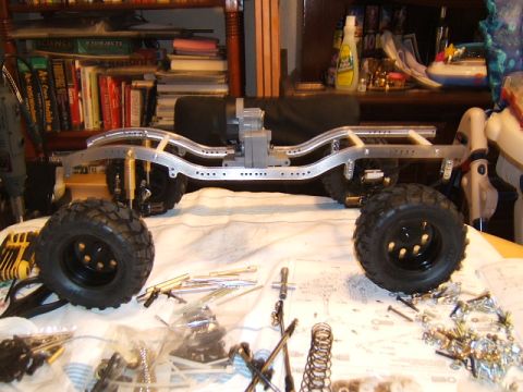 1988 Ford Bronco - The chassis of an RC crawler is shown with its suspension and tires, surrounded by various parts and tools.