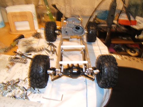 1988 Ford Bronco - An RC crawler chassis is assembled on a table, surrounded by tools and small parts.