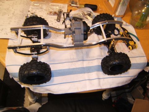 1988 Ford Bronco - The chassis of an RC crawler is shown with its gearbox and four tires, resting on a striped towel.