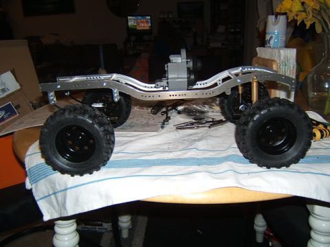 1988 Ford Bronco - The frame of a remote-controlled crawler vehicle is assembled on a table, showing its suspension and drivetrain components.