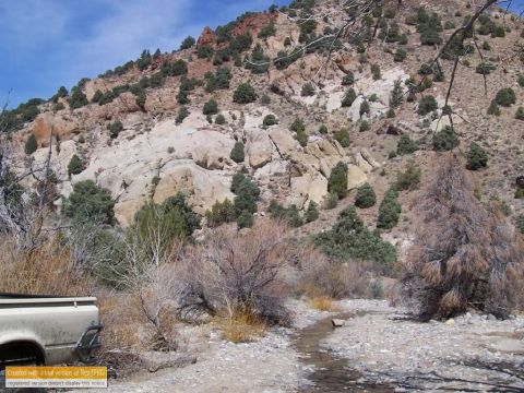 1986 Ford Bronco - A white pickup truck is partially visible in a dry, rocky environment with a small stream flowing nearby.