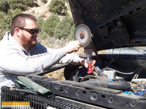 1986 Ford Bronco - Man uses a grinder on a car engine while working outdoors.