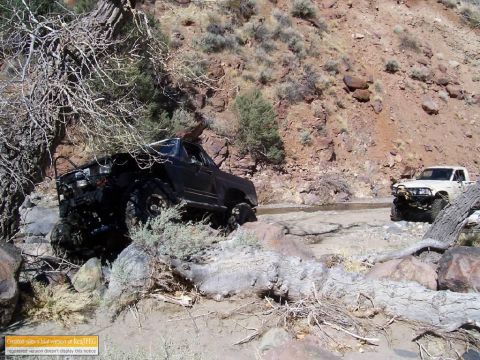 1986 Ford Bronco - Two off-road vehicles navigate a challenging rocky path in a desert landscape.
