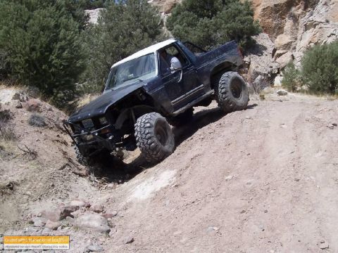 1986 Ford Bronco - Off-road Bronco navigating a steep, rocky incline on a dirt trail.