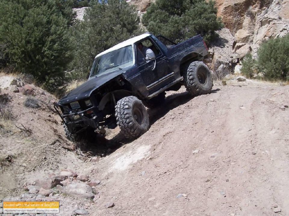 Modified black Ford Bronco with large tires climbing a dirt hill