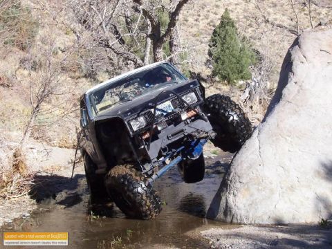 1986 Ford Bronco - Modified off-road vehicle tackles a challenging rocky terrain with water and mud.