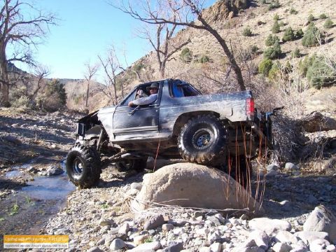 1986 Ford Bronco - This heavily modified truck navigates a rocky obstacle on a dry creek bed.