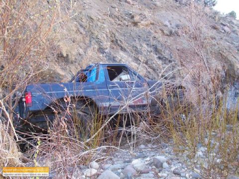 1986 Ford Bronco - This vehicle appears to be stuck in a rocky, brush-filled ravine, with visible damage to its roof.
