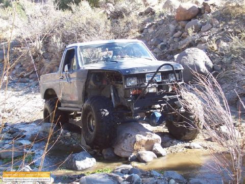1986 Ford Bronco - This heavily modified 1980s Ford Bronco is shown tackling a challenging off-road course with large tires and a lifted suspension.