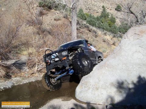 1986 Ford Bronco - This modified SUV is shown tackling a challenging off-road obstacle, with one wheel high on a large rock.