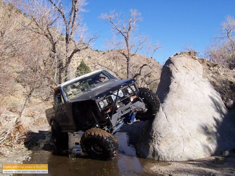Black off-road SUV with large tires navigating a rocky stream, front right tire on a boulder