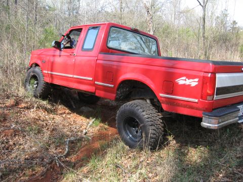 1995 Ford F-150 - A red 1995 Ford F-150 navigates an off-road trail with its large tires.
