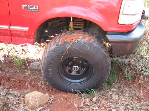 1995 Ford F-150 - Close-up of the front wheel and fender of a red Ford F-150 XLT, covered in mud and dirt.