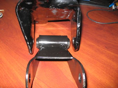 1991 Ford Bronco - A black metal suspension component with a rubber bushing is shown against a wooden background.