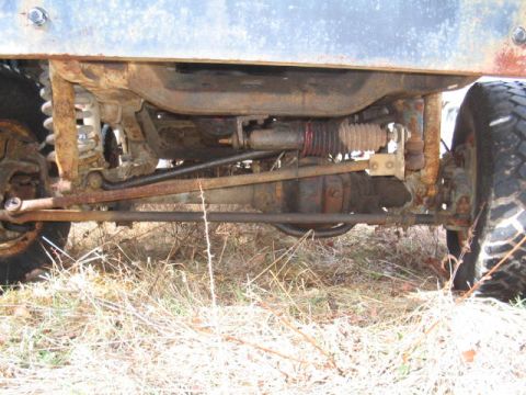 1979 Ford Bronco - Close-up of the rusty undercarriage and suspension system of a vehicle, with dry grass in the foreground.