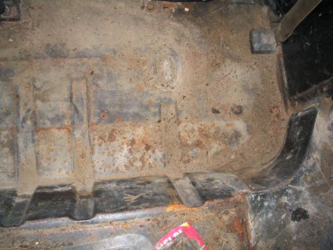 1979 Ford Bronco - Close-up of a heavily rusted vehicle floor pan, showing wear and debris.