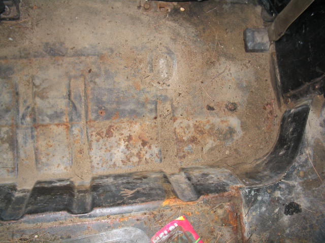 rusted floor pan with debris and some black plastic trim
