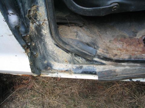 1979 Ford Bronco - The interior floor and door sill of a white vehicle exhibit extensive rust and deterioration.