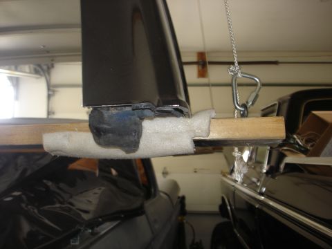 1979 Ford Bronco - A black car part is held by a rope and carabiner, with a wooden support underneath, in a garage setting.