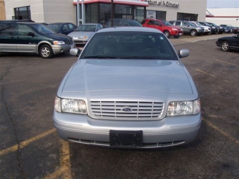 2003 Ford Crown Victoria - A silver 2003 Ford Crown Victoria is parked in front of a building with other vehicles visible.