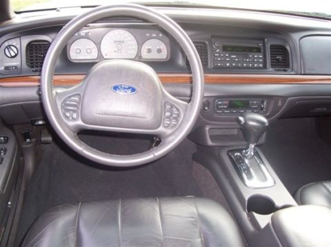 2003 Ford Crown Victoria - The interior of a 2003 Ford Crown Victoria, a leather-wrapped steering wheel and wood grain accents on the dashboard.