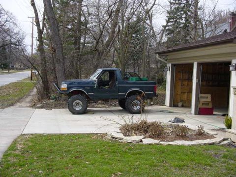 1992 Ford Bronco - A modified 1992 Ford Bronco sits parked on a concrete driveway next to a residential garage.