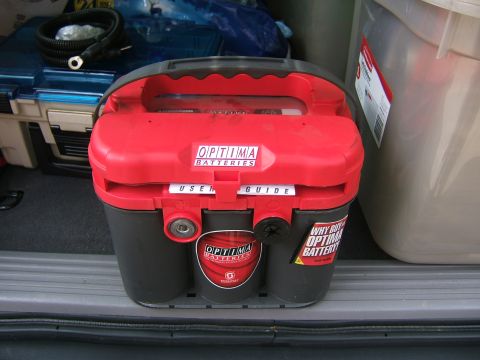 1991 Ford Bronco - A new Optima red-top spiral-cell battery with its red carry handle and 'USER GUIDE' label still attached, sitting on a vehicle's cargo sill…